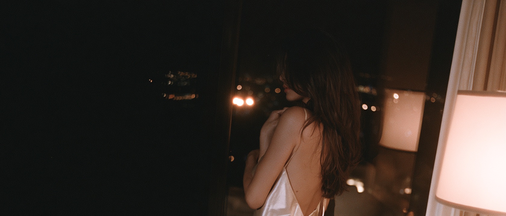 Advertiser in a silk slip at a night window over city lights